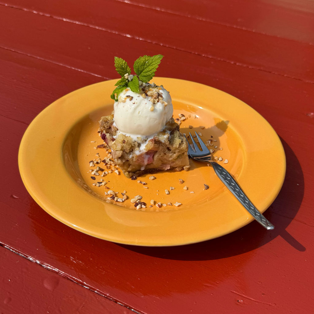 Ein Stück hausgemachter Bio-Kuchen mit Vanilleeis, serviert in unserem Gartencafé Gæsteriet. Wir bieten auch Kaffee, Bier, Wein und klassisch dänisches Smörrebröd an.